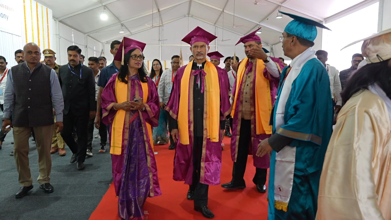 Dignitaries in ceremonial robes walking a red carpet under a marquee at a convocation ceremony